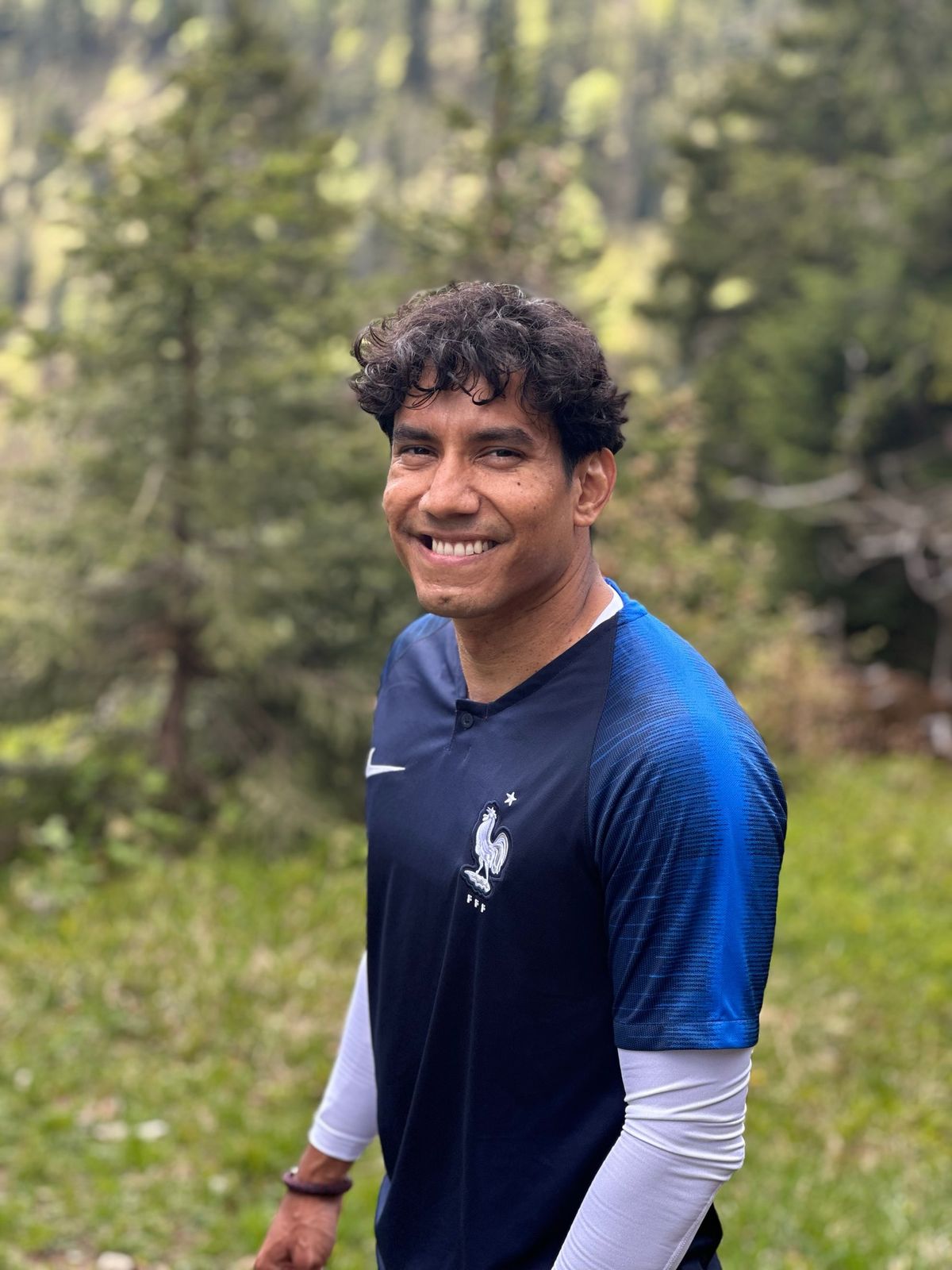 Portrait of Aldo smiling outdoors, standing among pine trees in the mountains
